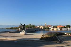 Die auf einer künstlich geschaffenen Insel liegende Altstadt von Nin ist durch zwei Brücken (eine davon hier im Bild) mit dem Festland verbunden. Die Statue zeigt den Fürsten Branimir, den ersten gesetzlichen Herrscher eines unabhängigen kroatischen Staates.