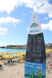 Maho Beach: Ein in den Sand eingelassenes Surfbrett dient als Tafel und zeigt die nächsten Landeanflüge an, denn hier wollen alle Gäste das gleiche: Das Super-Selfie mit Düsenjet!