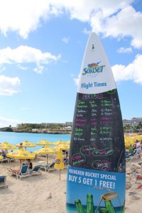 Maho Beach: Ein in den Sand eingelassenes Surfbrett dient als Tafel und zeigt die nächsten Landeanflüge an, denn hier wollen alle Gäste das gleiche: Das Super-Selfie mit Düsenjet! 