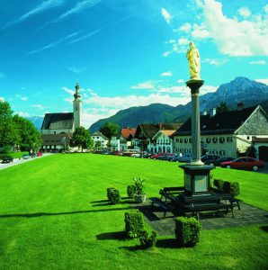 Der Dorfanger, nach dem die Gemeinde benannt ist, wird umrahmt von der mächtigen Pfarrkirche und der 1884 in Achthal gegossenen Mariensäule. - Foto: Berchtesgadener Land Tourismus