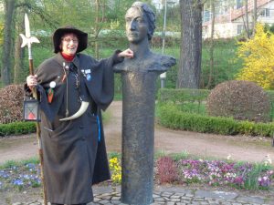 : Heiligenstadts Nachwächterin Heidelinde Liepe steht neben dem Denkmal von Heinrich Heine, das im Kurpark seinen Platz gefunden hat. Der Dichter (1797 – 1856) ließ sich in Heiligenstadt taufen. Er wählte diesen Ort, weil er die Taufe geheim halten wollte. – Foto: Dieter Warnick