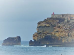 Die Felsenspitze mit dem Leuchtturm, Farol da Nazaré, ragt weit in das Meer und teilt den Strand in einen südlichen und nördlichen Teil.