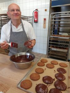 Nach dem die leckeren süßen Teilchen den Backofen verlassen haben, werden sie vom Chef höchstpersönlich mit einer feinen Zartbitter-Schokomasse überzogen. - Foto: Dieter Warnick