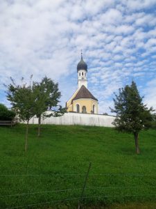 Oberbayerisches Idyll mit weiß-blauen Schäfchenwolken: die katholische Filialkirche Mariä Himmelfahrt in Jenhausen, einem Ortsteil von Seeshaupt; sie wurde um 1730 errichtet und liegt an exponierter Stelle auf einem Hügel oberhalb des Ortes. – Foto: Dieter Warnick