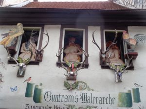 Üppig gebaute Damen blicken aus den Fenstern des ersten Stocks von „Guntrams Malerarche“ auf die Hauptstraße. – Foto: Dieter Warnick