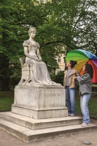 Mitten im grünen Herzen von Meran, eingebettet zwischen Passer und Palmen, thront eine elegante Marmorgestalt auf ihrem Sockel: die Statue der Kaiserin Elisabeth von Österreich, liebevoll „Sisi“ genannt. – Foto: Anita Rossi